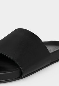 Μαύρο σανδάλι slide με φαρδιά μονή λουρίδα και επίπεδη σόλα, παρουσιάζεται σε απλό φωτεινό φόντο.