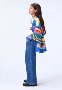 Colorful striped cardigan in soft, fuzzy knit, featuring shades of blue, orange, and green, paired with blue wide-leg jeans and black shoes.