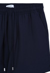 Pantaloni corti blu navy con vita elasticizzata e cordoncino. Dotati di tasche laterali e una superficie liscia e morbida. Etichetta con scritto 'CALLIOPE'.