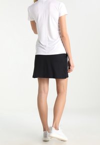 Vit kortärmad topp med en söm på ryggen, kombinerad med en svart kjol. Outfiten fulländas med vita sneakers med grå detaljer.