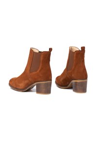 Botines de ante marrón con paneles laterales elásticos, punteras redondas y tacones apilados. Cuenta con una lengüeta en la parte trasera para facilitar el calzado.