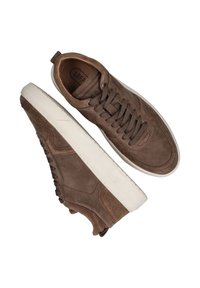 Bruine suède lage sneakers met een textuurafwerking, vlakke witte rubberen zool, en vetersluiting. Heeft zichtbare stiksels en een treklus aan de achterkant.