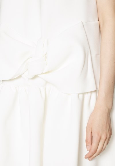 Bijela haljina od glatkog materijala s detaljem čvorastog remena na struku i mekom, nabranoj suknji. Materijal ima blagi sjaj.