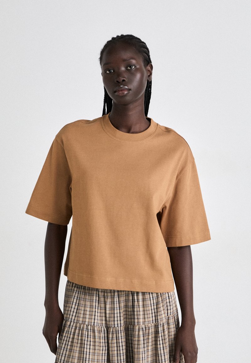 Brun kortermet bomulls t-skjorte med rund hals og avslappet passform, kombinert med et rutete, lagdelt skjørt i beige og brune toner.