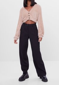 Beige fluffig kort cardigan med knappar framtill, tillsammans med högmidjade svarta vida byxor och kraftiga svarta ankelboots.