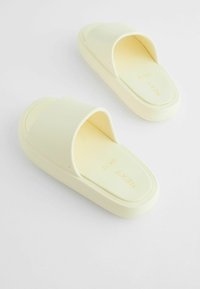 Sandales jaunes à enfiler avec une finition lisse et mate et de larges brides. La semelle intérieure présente le nom de la marque en relief ; bords arrondis et rembourrés.