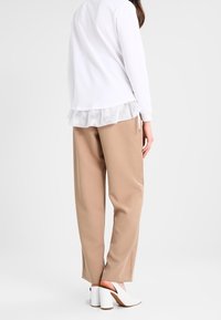 Vit långärmad topp med en mesh-volang i fållen, kombinerad med beige vida byxor. Skorna är vita klackar med blockdesign.