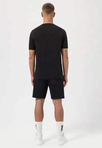 Svart t-shirt med kort ärm och svarta shorts, tillverkade av en mjuk bomullsblandning. Bärs med vita sneakers och ribbade strumpor som visar "BAIRD."