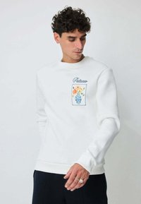 Sweatshirt blanc avec un imprimé floral sur la poitrine gauche, col rond et poignets et ourlet côtelés. Texture douce.