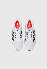Hvide atletiske sko med sorte detaljer, mesh-overdel, polstret krave og røde indlægssåler mærket "ADIDAS TRAINING." Har snørebånd og tekstureret sål.