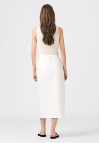 Bílá bavlněná midi sukně, s vysokým pasem a rovný střih, obsahující dvě zadní kapsy a jemnou texturu. Ve spojení s krémovým topem.