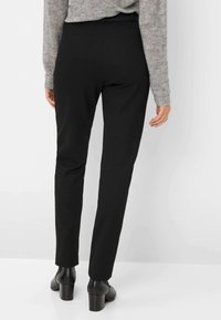 Pantaloni neri aderenti con una texture liscia, gambe affusolate e vita a media altezza, abbinati a stivali neri con tacco alla caviglia.