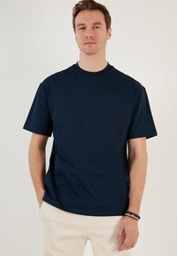 Tricou scurt din bumbac de culoare albastră închisă, cu guler rotund și croială relaxată, având o textură netedă și cusături minime.