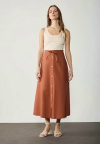 Rust-colored midi skirt with a fitted waist and bow detail, featuring a front button closure and A-line silhouette, made of lightweight fabric.