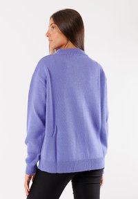 Maglione viola a maglia con vestibilità rilassata, colletto e polsini a coste, tessuto testurizzato e orlo dritto, indossato su pantaloni neri.