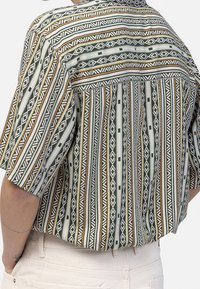 Short-sleeve shirt featuring vertical stripes in green, white, and brown with geometric patterns and a relaxed fit. Textured fabric detail.