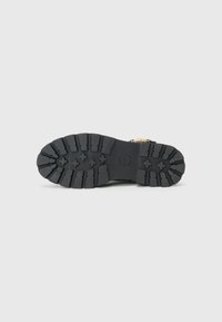 Suola di scarpa in gomma nera con un motivo di battistrada robusto, caratterizzato da scanalature profonde e un logo circolare al centro. Finitura resistente e ruvida.
