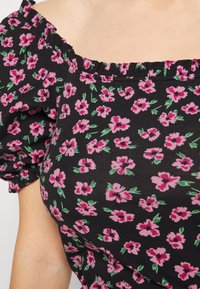 Top preto com padrão floral, apresentando flores rosa e verdes, com mangas curtas e bufantes e um decote rufado com ombros à mostra. Material de algodão.