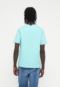 Ανοιχτό μπλε βαμβακερό μπλουζάκι με κοντά μανίκια και στρογγυλή λαιμόκοψη, φορεμένο με μπλε τζιν παντελόνι, με άνετη εφαρμογή και απλό σχέδιο.