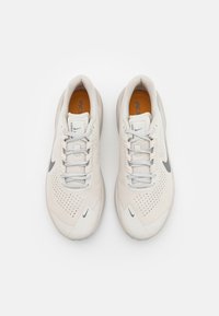 Scarpe da ginnastica bianche con una tomaia testurizzata, perforazioni traspiranti, accenti grigi e lacci piatti. Suola leggera per comfort e aderenza.
