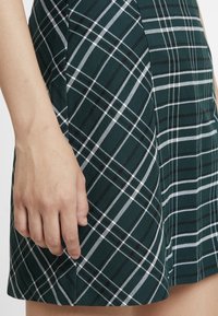 Jupe trapèze à carreaux verts avec des rayures blanches et noires. Le tissu semble texturé, avec une taille ajustée et des poches latérales.