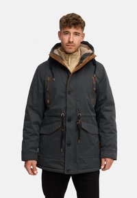 Donkergroen parka-jacket met een capuchon gevoerd met bruin imitatieschapenbont, steekzakken aan de voorkant, een taillekoord en knoopsluitingen, met contrasterende stiksels.