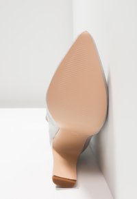 Chaussure à talon haut argentée avec une surface lisse et un bout pointu. La semelle est beige avec des rainures, se rétrécissant vers l'arrière, révélant des accents minimaux.