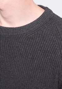 Maglione grigio scuro in maglia con una texture a coste e un colletto tondo. Vista ravvicinata che mette in risalto il suo materiale e le cuciture.