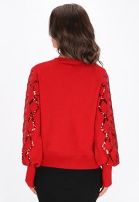 Czerwony sweter z cekinowym wzorem diamentów na rękawach, dopasowane wykończenie i okrągły dekolt. Miękka faktura i dzianinowy materiał.