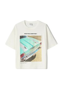 T-shirt blanc en coton avec un graphisme de voiture vintage en turquoise et argent, accompagné de texte en noir au-dessus et en dessous de l'image.