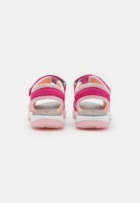 Roze sandal s mrežastimi trakovi in nastavljivimi zaponkami, ki ima oblazinjeno notranjost in kontrastno belo-roza podplat.