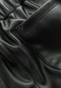 Nærbillede af sort læderstof med detaljeret syning og samlet elastisk sektion.