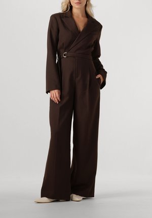 Combinaison brune sur mesure avec col cranté, manches longues, taille ceinturée et jambes larges, confectionnée dans un tissu texturé.