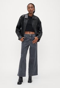 Svart faux skinnjakke over en svart crop top, parret med grå vid bukser med en subtil teksturert stripemønster. Svart platåstøvler.