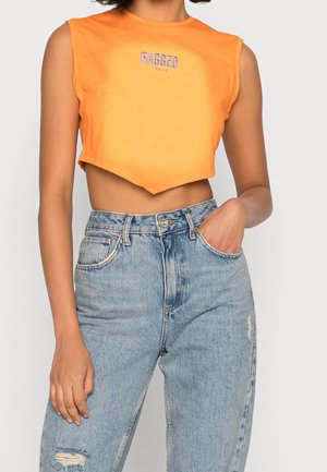Orangenes, cropped ärmelloses Top mit strukturierter Oberfläche und lila Aufschrift "RAGGED JEANS". Kombiniert mit hellblauen, distressed Jeans.