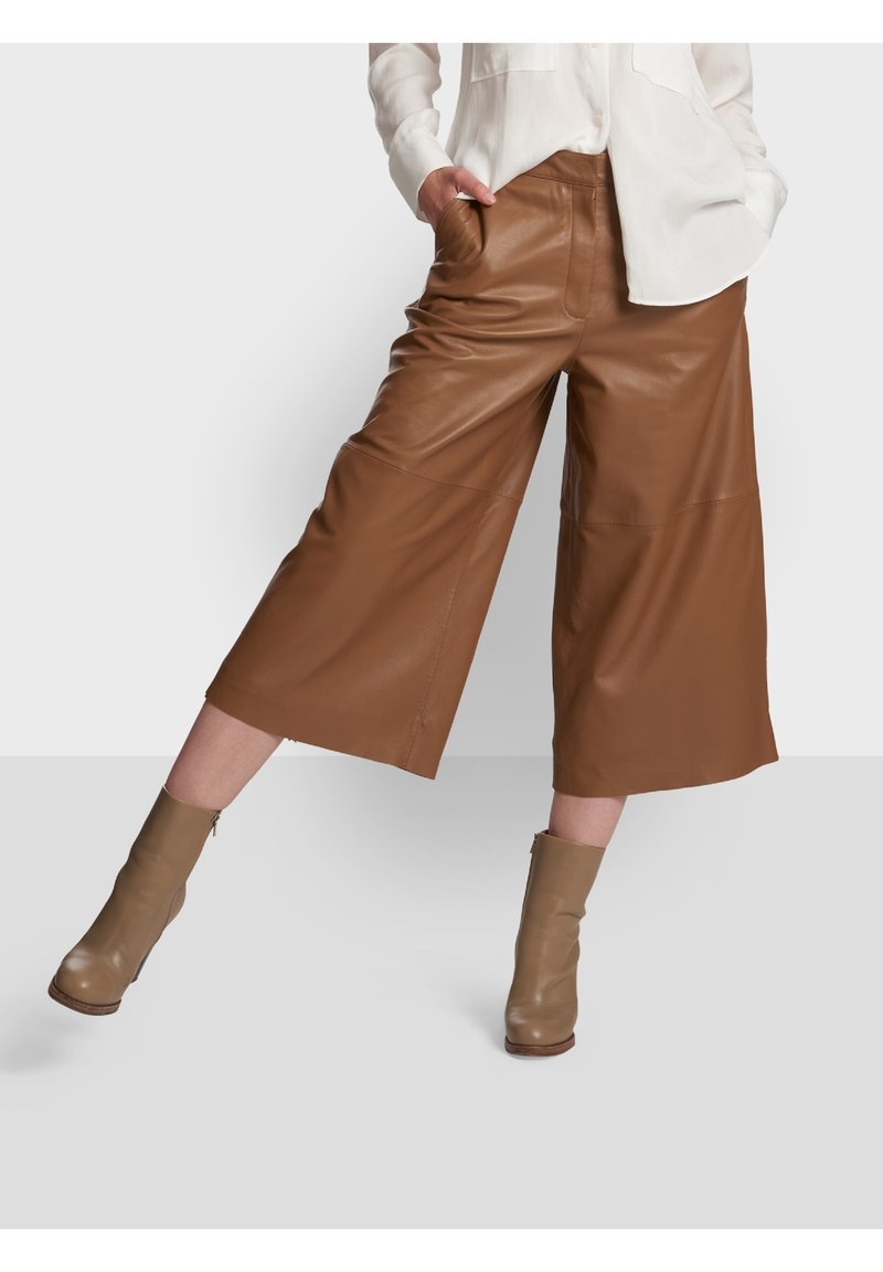 Brązowe skórzane spodnie culotte z dużymi przednimi kieszeniami, charakteryzujące się szerokim krojem nogawek. W połączeniu z taupe'owymi botkami za kostkę. Gładka tekstura, minimalne detale.