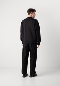 Sudadera negra con cuello redondo, combinada con pantalones cargo negros que tienen bolsillos laterales y botones a presión. Textura suave, ajuste relajado.