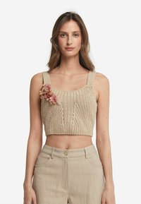 Beige stickad croptop med breda axelremmar och en blommig detalj, som har ett strukturerat mönster och en ribbad halsringning.