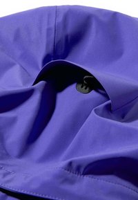 Lila színű anyag sima textúrával, húzózsinóros záródással és középen egy kerek fekete műanyag rögzítővel.