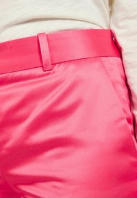 Pantalons en satin rose vif, présentant une texture lisse et une taille simple avec une passant de ceinture, montrés de la taille vers le bas.