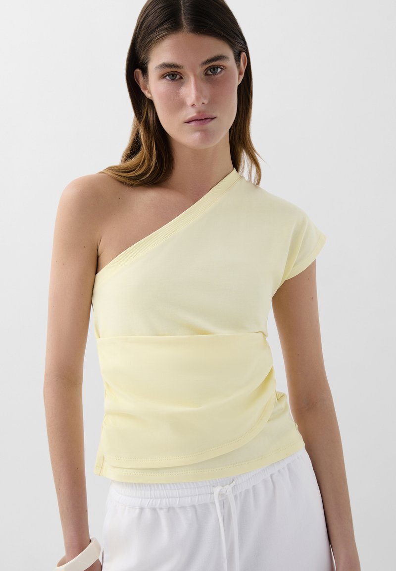 Asymmetrisk gul topp laget av myk, elastisk stoff; har en enkelt cap-sleeve og rynkedetalj i midjen.