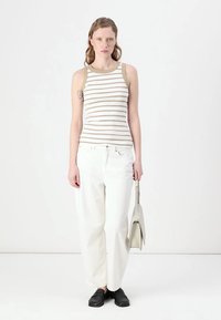 Stripet tanktop med krem- og beige farger, kombinert med hvite, løse jeans og svarte slip-on sko, holder en lys grå veske.