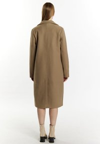 Beige vlněný kabát se strukturovanou siluetou, klopovým límcem a rovný řez. Má dlouhé rukávy a středový šev na zadní straně.