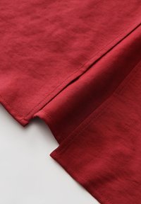 Roter Baumwollstoff, glatte Textur, mit sauberer Naht und gefaltetem Rand. Subtile Farbvariationen und leichter Glanz sind sichtbar.