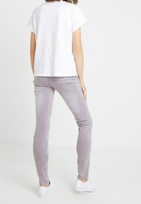 Vit kortärmad t-shirt i kombination med figurnära, vertikalt randiga byxor i grått och vitt, kompletterat med vita sneakers.