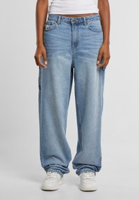 Světlé modré oversized džíny s rovnými nohavicemi, s předními kapsami a zapínáním na knoflíky. Stylizované s bílými teniskami.