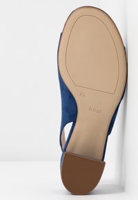 Semelle d'une chaussure plate en daim bleu avec un petit talon marron, taille 4½, et le nom de la marque « högl » embossé sur la semelle beige.