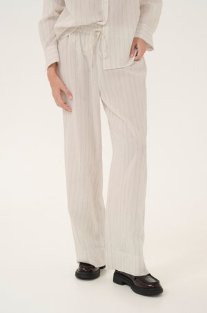 Linen blend outfit with vertical stripes; lightweight long-sleeve top and loose-fitting pants in light beige. Black platform shoes.