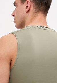 Maslinasto zelena Nike Pro majica bez rukava, izrađena od glatkog, elastičnog materijala. Ima diskretni logo na leđima i ravne šavove za udobnost.