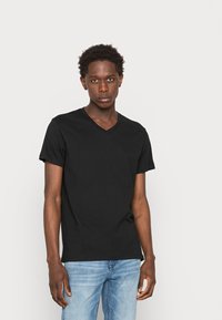 Camiseta de algodón negra con cuello en V y mangas cortas, textura suave, diseño ajustado, combinada con jeans de mezclilla azul claro.